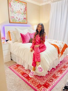 a woman sitting on top of a white bed in a room with pink and orange decor