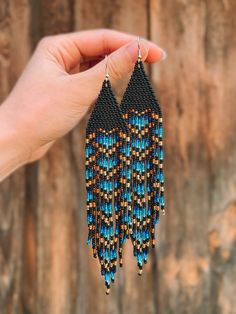 a hand holding up a pair of beaded earrings with blue and brown beads on it