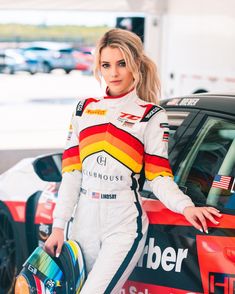 a woman in a racing suit standing next to a car