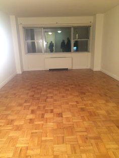 an empty room with hard wood flooring and two people standing in the window sill