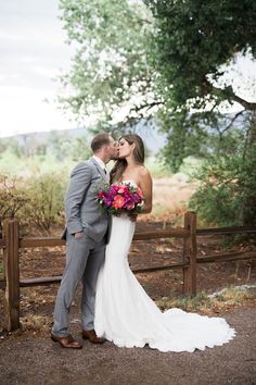 a bride and groom kissing in front of a wooden fence at their outdoor wedding venue