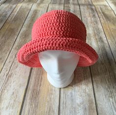 a white mannequin head wearing a red crocheted hat on top of a wooden floor