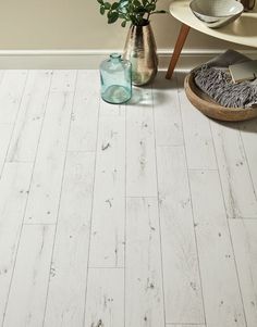 a white wood floor with vases and flowers on the side table next to it