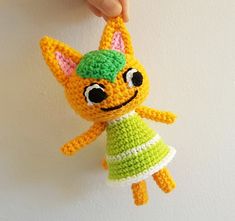 a crocheted cat hanging from a wall with a hand holding the keychain