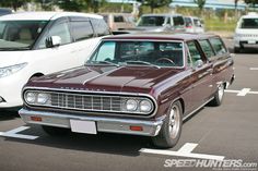 a maroon station wagon parked in a parking lot next to other cars and vans on the street