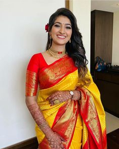 a woman in a yellow and red sari with her hands on her hips smiling