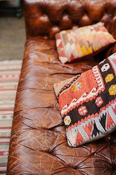 two pillows are sitting on the back of a brown leather couch in a living room