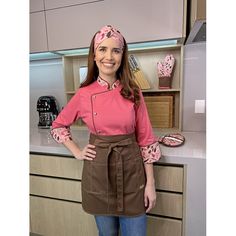 a woman standing in front of a kitchen counter wearing a pink shirt and brown apron