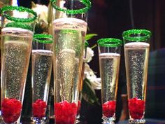 four champagne flutes filled with red and green liquid sitting on a table next to flowers