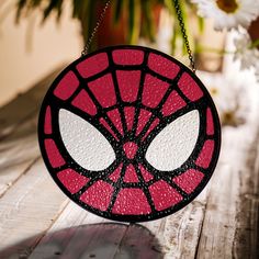 a spider - man stained glass hanging decoration on a wooden table with daisies in the background