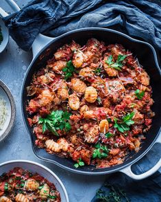 a skillet filled with pasta and shrimp next to two bowls full of white rice