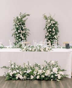 the table is set with white flowers and greenery, candles are on each side