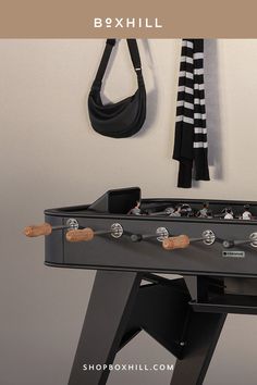 Close up view of a black outdoor football table with wooden handles placed against a minimalist light colored wall