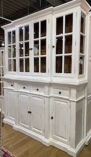 a white china cabinet with glass doors on the top and bottom, in a store