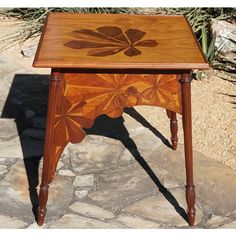 a wooden table with an intricate design on it's top and bottom edge, sitting in front of a cactus