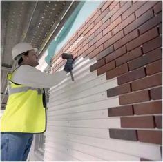 a man in safety vest and hard hat working on a brick wall with a drill