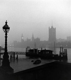 a black and white photo of boats in the water near a light pole with a clock on it