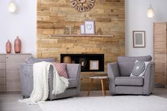 a living room with two gray chairs and a clock on the wall above it's fireplace