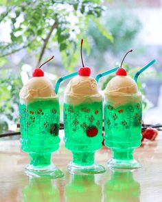 three plastic cups with ice cream and cherries on them, sitting on a table