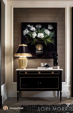 a black and gold sideboard with white flowers on it in front of a painting