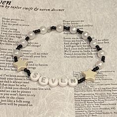 a bracelet with beads and charms that say seven written in white, black and silver