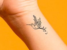 a small tattoo on the wrist of a woman's arm with a bird flying above it