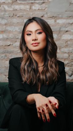 a woman sitting on top of a green couch wearing a black suit and red nail polish