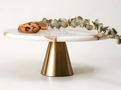 a white and gold cake stand with cookies on it's top, surrounded by leaves