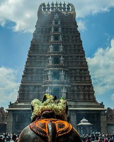 an elephant with flowers on it's head in front of a tall tower structure