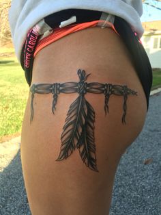 a woman's thigh with a cross and feathers tattoo on the side of her leg