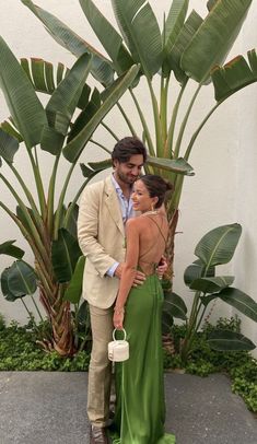 a man and woman standing next to each other in front of some palm tree leaves