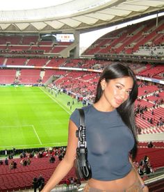 a woman standing in front of a soccer field with her hand on her hip and looking at the camera