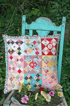 a colorful patchwork pillow sitting on top of a wooden chair in front of some bushes