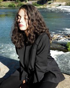 a woman sitting on top of a rock next to a river