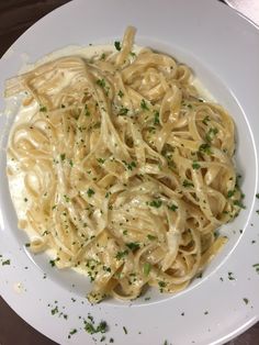 a white plate topped with pasta covered in sauce and garnished with parsley