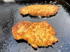 two pieces of fried chicken cooking in a pan on the stove top with water droplets