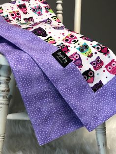 two purple owls and polka dots are on the back of a white chair with a blue blanket