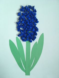 a blue flower cut out of paper sitting on top of a white surface with green leaves