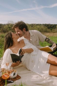 a man and woman are sitting on the grass with an open book in their hands