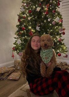 a woman sitting in front of a christmas tree holding a teddy bear