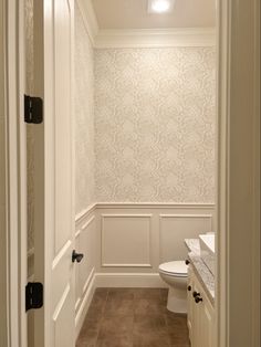 a white toilet sitting inside of a bathroom next to a wallpapered wall behind it