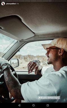 a man driving a car with his hand on the steering wheel while wearing a hat