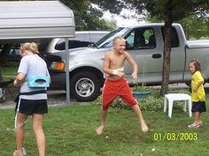 a group of people playing frisbee in the grass next to a truck and camper