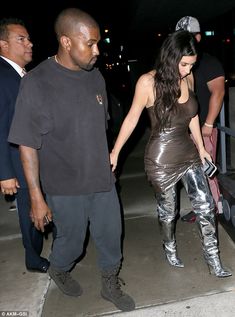 a man and woman are walking down the street together, one is wearing shiny silver leggings