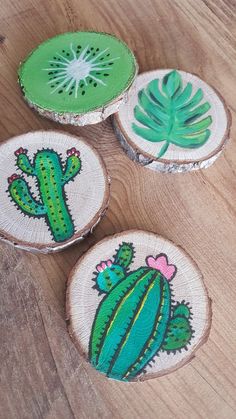 three wooden slices with green and pink designs on them sitting on a wood floor next to a plant