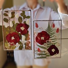 two red flowers are hanging from the side of a glass block with leaves and flowers on it