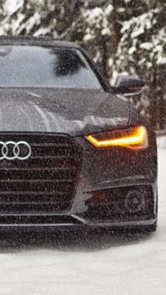 an audi car driving on a snowy road in the snow with its headlights turned down