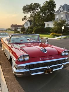 an old red car is parked on the side of the road in front of some houses