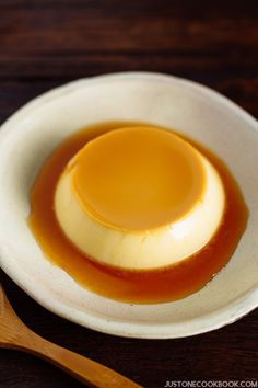 a white bowl filled with caramel sauce on top of a wooden table next to a spoon