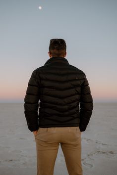 a man standing in front of the ocean looking at the moon and stars above him